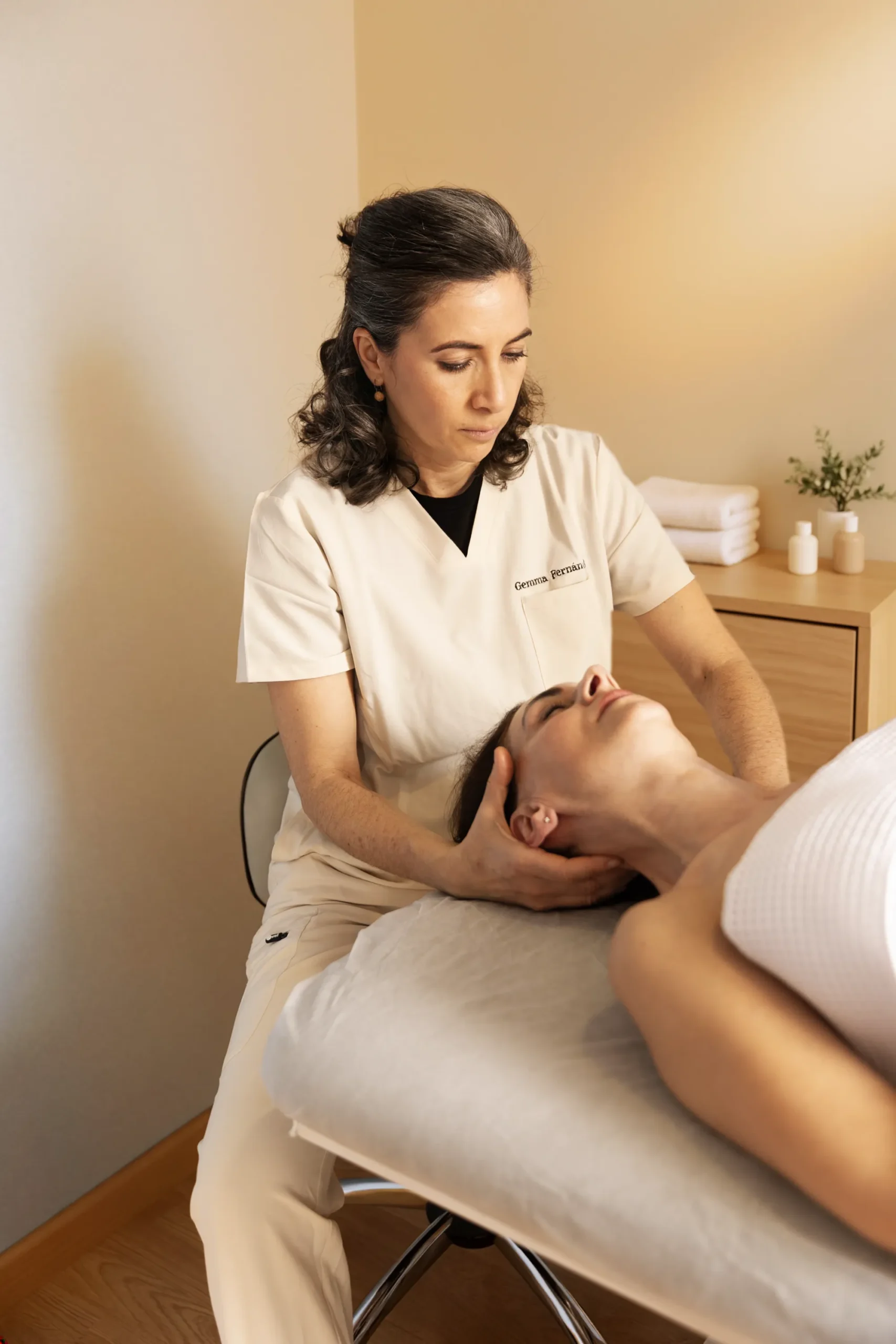 Gemma Fernández performing a cervical physical therapy maneuver on a patient lying on a treatment table.