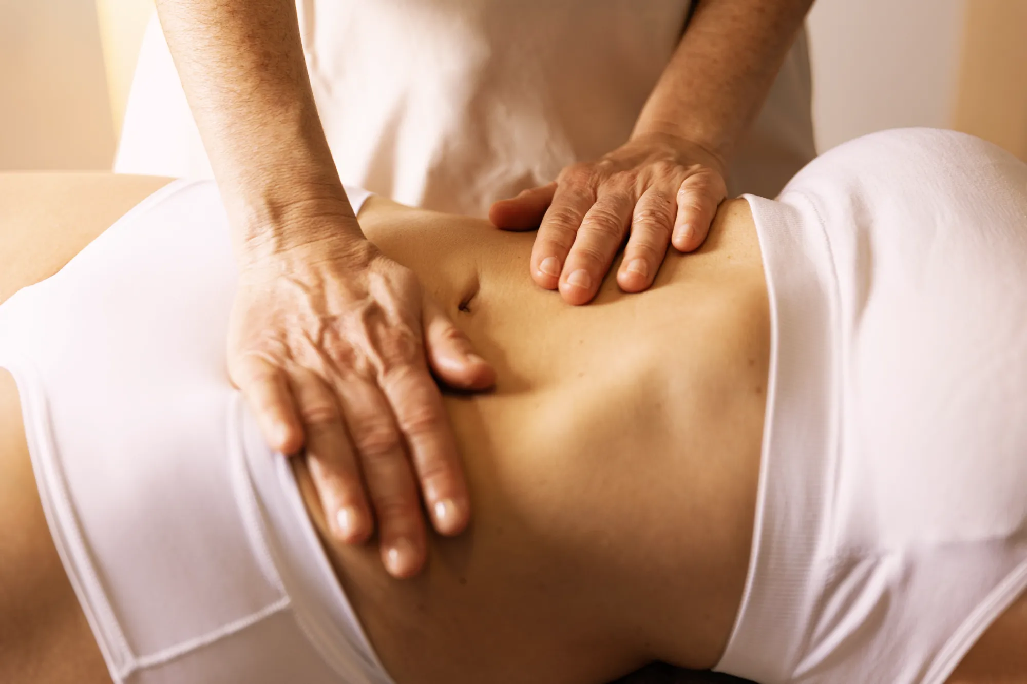 Manos de la fisioterapeuta aplicando un masaje de drenaje linfático en el abdomen de una paciente.