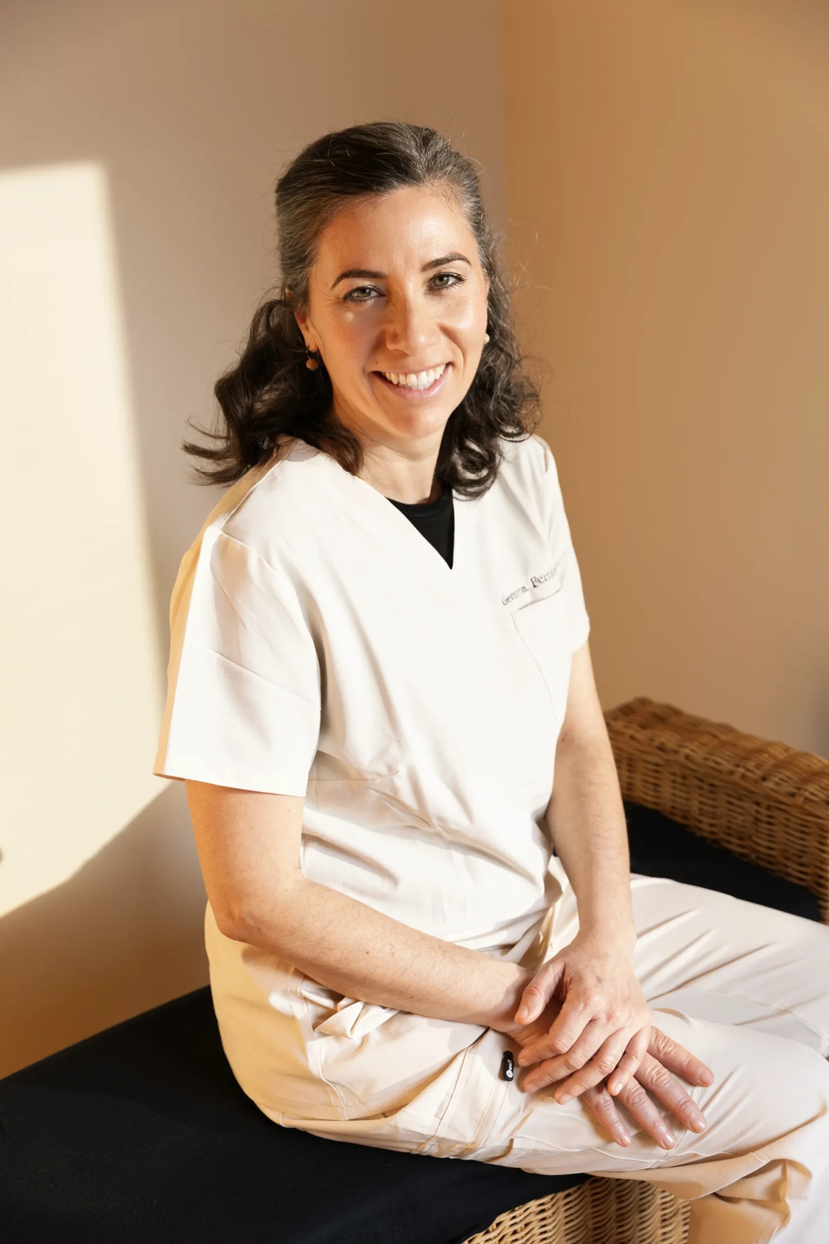 Gemma Fernández, fisioterapeuta, sentada y sonriendo con uniforme sanitario en su consulta.
